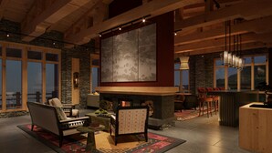 A cozy interior with a fireplace, wooden beams, stone walls, and large windows offering views.