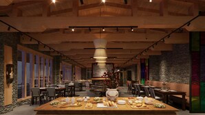A restaurant with a central wooden table set with various dishes, surrounded by chairs and tables.