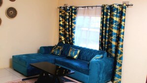 Un salon avec un canapé bleu, une table basse et des rideaux à motifs.