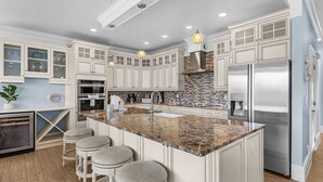 A modern kitchen with white cabinetry, a central island with stools, stainless steel appliances, and pendant lighting. - 571 Seabatical: Canal Front With Pool! (Fort Myers Beach)