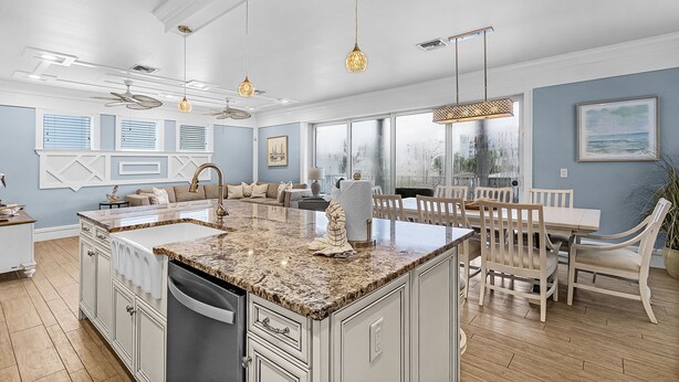 A spacious kitchen with a large island, white cabinetry, and a dining area with wooden chairs and a table. - 571 Seabatical: Canal Front With Pool! (Fort Myers Beach)