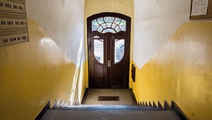 Un escalier menant à une porte ornée d’un vitrail, flanqué de murs jaunes et d’une rampe d’escalier en métal.