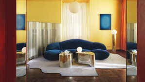 Un salon moderne avec un canapé bleu, deux tables d’appoint métalliques et un tapis blanc.