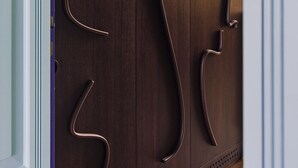 Une porte en bois sombre ornée de poignées aux motifs abstraits et découpés.