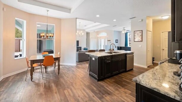 Une cuisine spacieuse avec des meubles de couleur sombre, un îlot central et un coin repas doté de chaises orange.