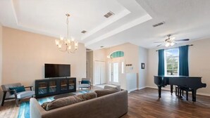 Un salon spacieux avec un grand piano noir, un canapé confortable, un téléviseur à écran plat et un lustre.