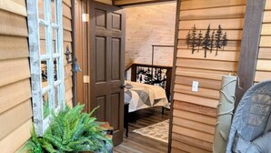 A cozy cabin interior with a wooden exterior, a bed with a geometric-patterned bedspread, a chair, and a wall-mounted clock. - Bar Harbor Cabin with Treehouse Suite & Hot Tub (Hancock)