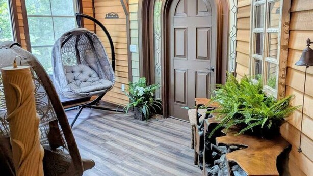 A cozy interior with a wooden ceiling, a large arched door, a hanging chair, and a rustic wooden table with plants. - Bar Harbor Cabin with Treehouse Suite & Hot Tub (Hancock)