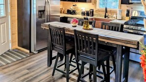 A kitchen with a central island, black chairs, a stainless steel refrigerator, and a stove. - Bar Harbor Cabin with Treehouse Suite & Hot Tub (Hancock)