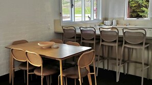 Un comedor con una mesa y sillas, una ventana con vista a follaje, y una zona de cocina con un lavamanos y encimera.