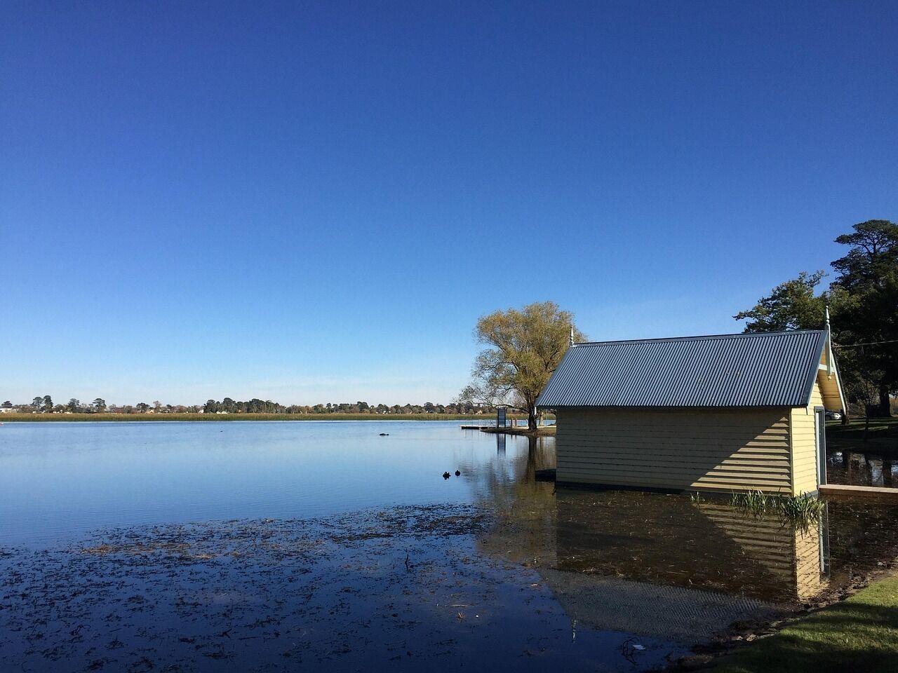 A calm lake with a wooden boathouse and a dock extending into the water.