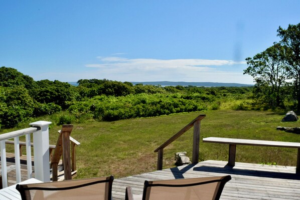 A deck with outdoor seating and a view of a grassy area with trees and distant mountains.