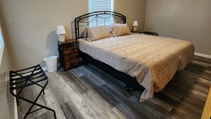 A bedroom with a bed, bedside tables, a window, and a small stool. - Hammond Hideaway, Lovely cabin 12 miles north of Fort Scott. (Fort Scott)