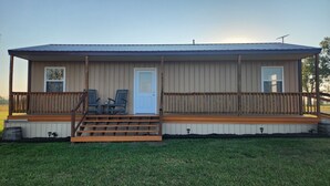A single-story building with a porch, two windows, a door, and a small outdoor seating area with two chairs. - Hammond Hideaway, Lovely cabin 12 miles north of Fort Scott. (Fort Scott)