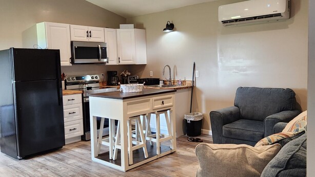 A compact living space with a kitchenette, a black refrigerator, a microwave, a coffee maker, a sink, and a grey sofa. - Hammond Hideaway, Lovely cabin 12 miles north of Fort Scott. (Fort Scott)