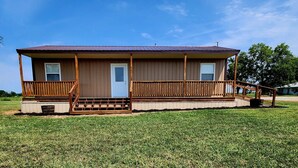 A single-story wooden house with a porch, a front door, and a small front yard. - Hammond Hideaway, Lovely cabin 12 miles north of Fort Scott. (Fort Scott)