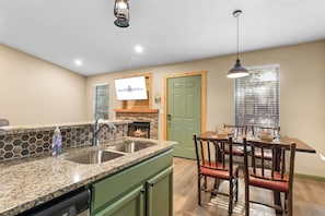 A kitchen with a stone countertop, a sink, a dining table with chairs, and a green door.