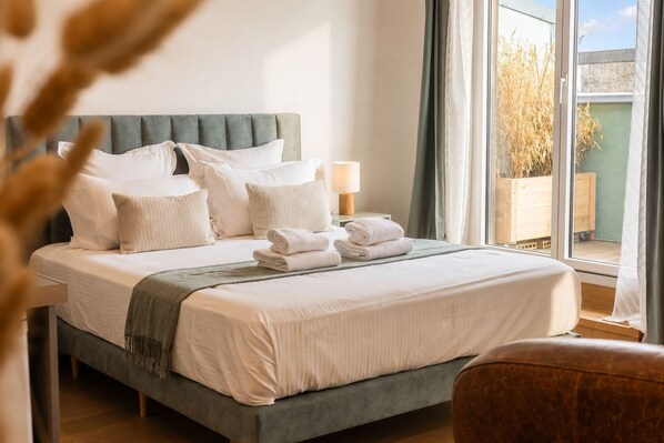 A neatly made bed with pillows and folded towels, a bedside lamp, and a view of the outdoors through a window.