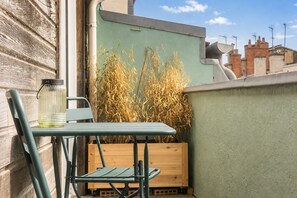 A small outdoor seating area with a table and chairs, a wooden crate, and a glass container on a balcony.