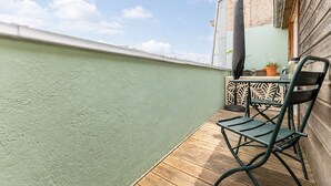 A balcony with a green wall, a wooden floor, a metal chair, a table with a potted plant, and a decorative panel. - Bright Apartment in the City Centre, Terrace, A/C (Bordeaux)