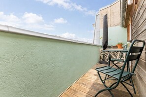 A balcony with a green wall, a wooden floor, a metal chair, a table with a potted plant, and a decorative panel. - Bright Apartment in the City Centre, Terrace, A/C (Bordeaux)