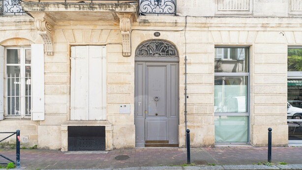 A building with a stone facade, a grey door with an ornate arch, and a window with a metal grill. - Bright Apartment in the City Centre, Terrace, A/C (Bordeaux)