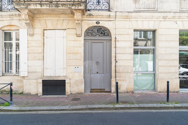 A building with a stone facade, a grey door with an ornate arch, and a window with a metal grill.