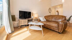 A modern living room with a leather sofa, a flat-screen TV, a small round table, and a wicker side table. - Bright Apartment in the City Centre, Terrace, A/C (Bordeaux)