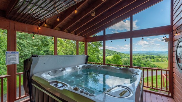 Een hottub op een houten terras met uitzicht op een bergachtig landschap.
