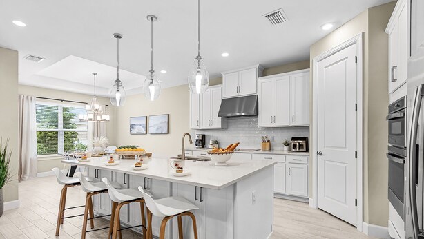 Une cuisine moderne dotée d’un grand îlot central, de luminaires suspendus et de meubles blancs.