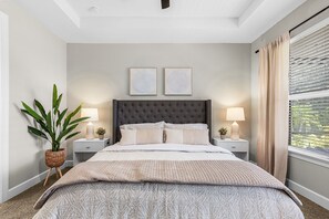 A bedroom with a tufted headboard, a large bed with multiple pillows, two bedside tables with lamps, a potted plant, and a window with curtains. - Charming, Comfort and Relaxation Await! - Casa Bella - Roelens (Cape Coral)