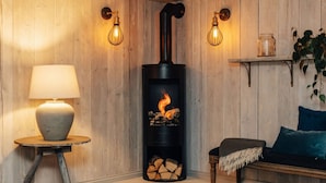 Een gezellige kamer met een houtkachel, een lamp, een plank met een plant en een bank.
