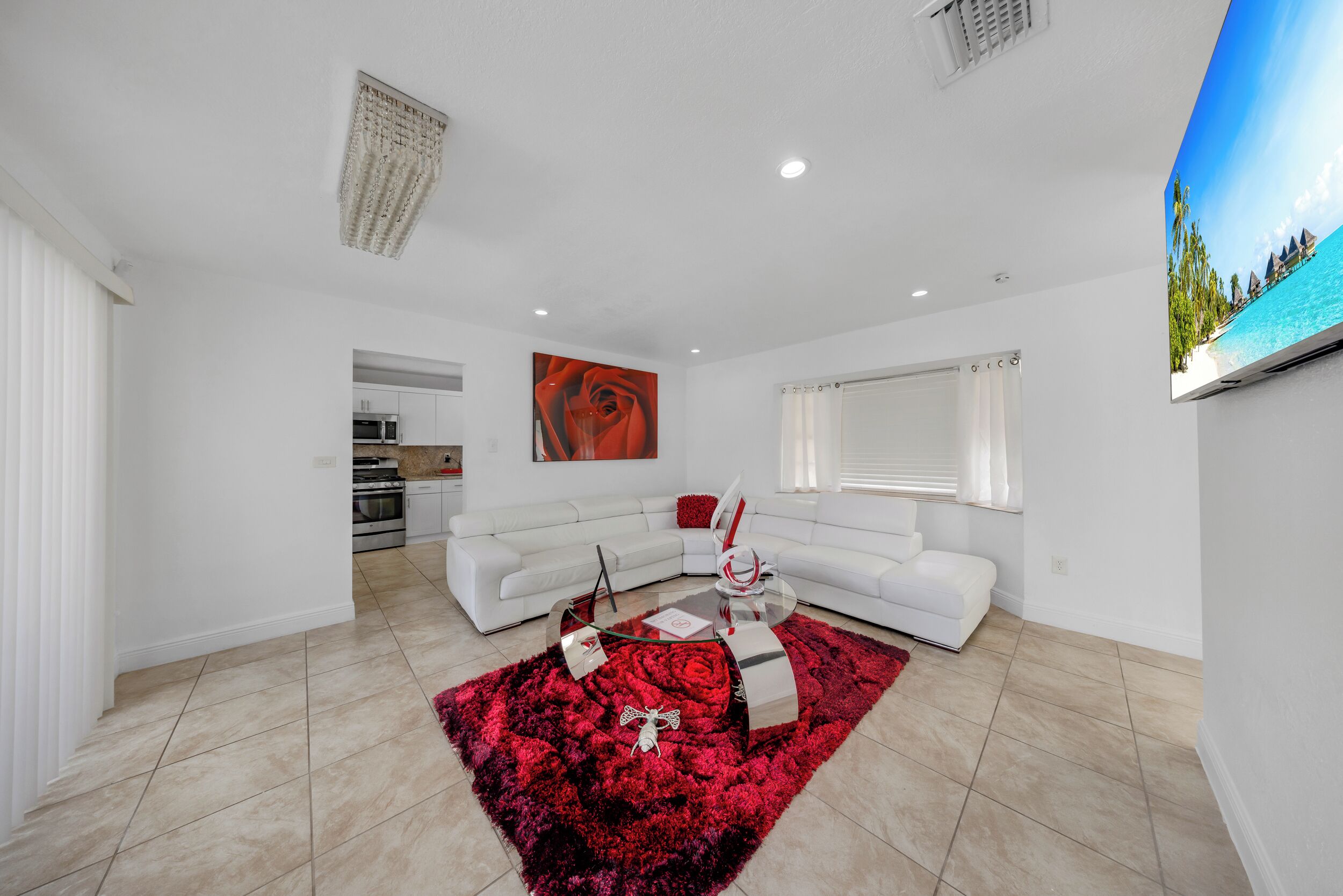 A modern living room with a white sectional sofa, a glass coffee table, and a red shag rug.