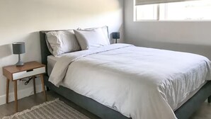 A bedroom with a bed, nightstand, lamp, and a window with blinds. - Stylish Comfy 4-Bedroom House in Anaheim - Close to Disney! (Anaheim)