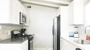 A modern kitchen with white cabinetry, a black refrigerator, a stove, a microwave, and a blender on the countertop. - Stylish Comfy 4-Bedroom House in Anaheim - Close to Disney! (Anaheim)