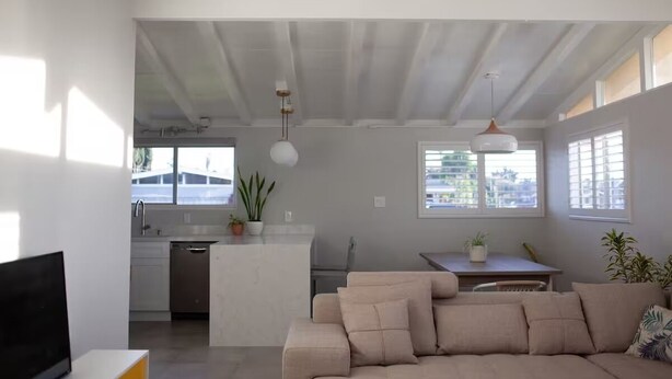 A modern living room with a beige sofa, a flat-screen TV, and a dining area with a table and chairs. - Stylish Comfy 4-Bedroom House in Anaheim - Close to Disney! (Anaheim)