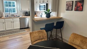 A modern kitchen with white cabinets, a stainless steel dishwasher, and a wooden countertop. There is a dining area with a black table and two blue chairs. - Zen Garden Bungalow close to Downtown (Chattanooga)