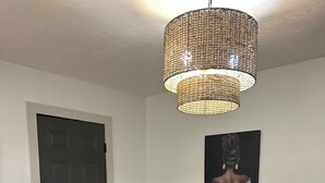 A dining area with a round table, four chairs, a woven pendant light, a door, and a framed artwork on the wall. - Zen Garden Bungalow close to Downtown (Chattanooga)