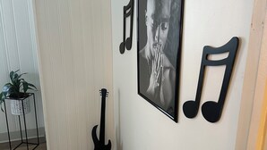 A room with a wooden floor, a black guitar, a framed photograph, and two black musical notes on the wall. - Zen Garden Bungalow close to Downtown (Chattanooga)