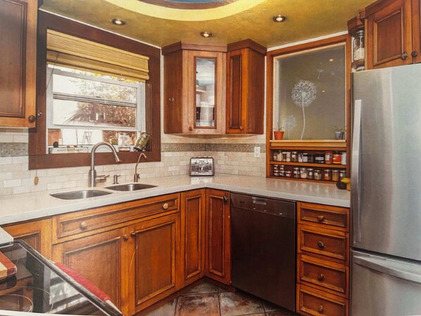 A kitchen with wooden cabinets, a stainless steel refrigerator, a built-in dishwasher, and a window with a view of the outside.