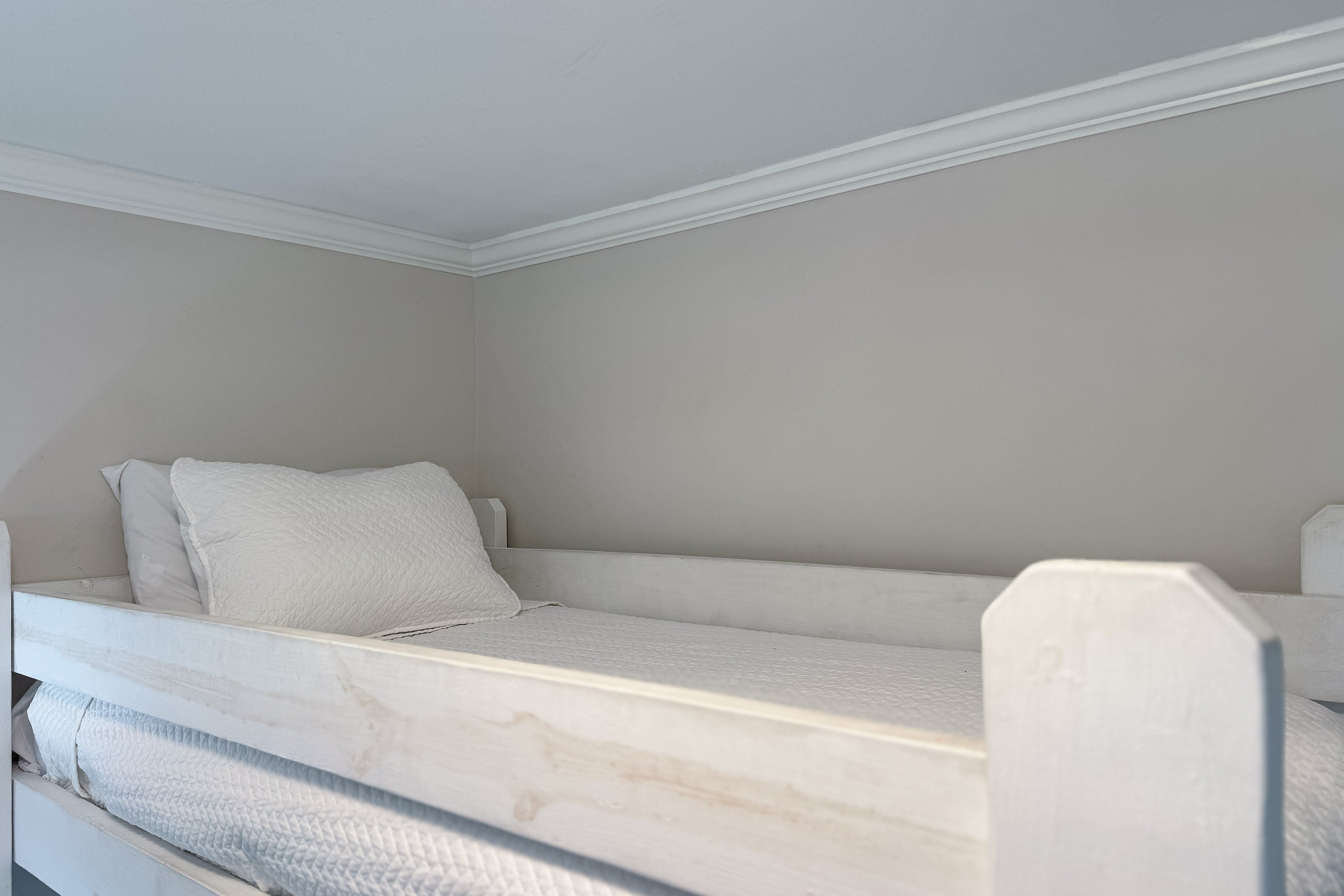A bunk bed with a mattress and pillows, white walls, and a white ceiling.