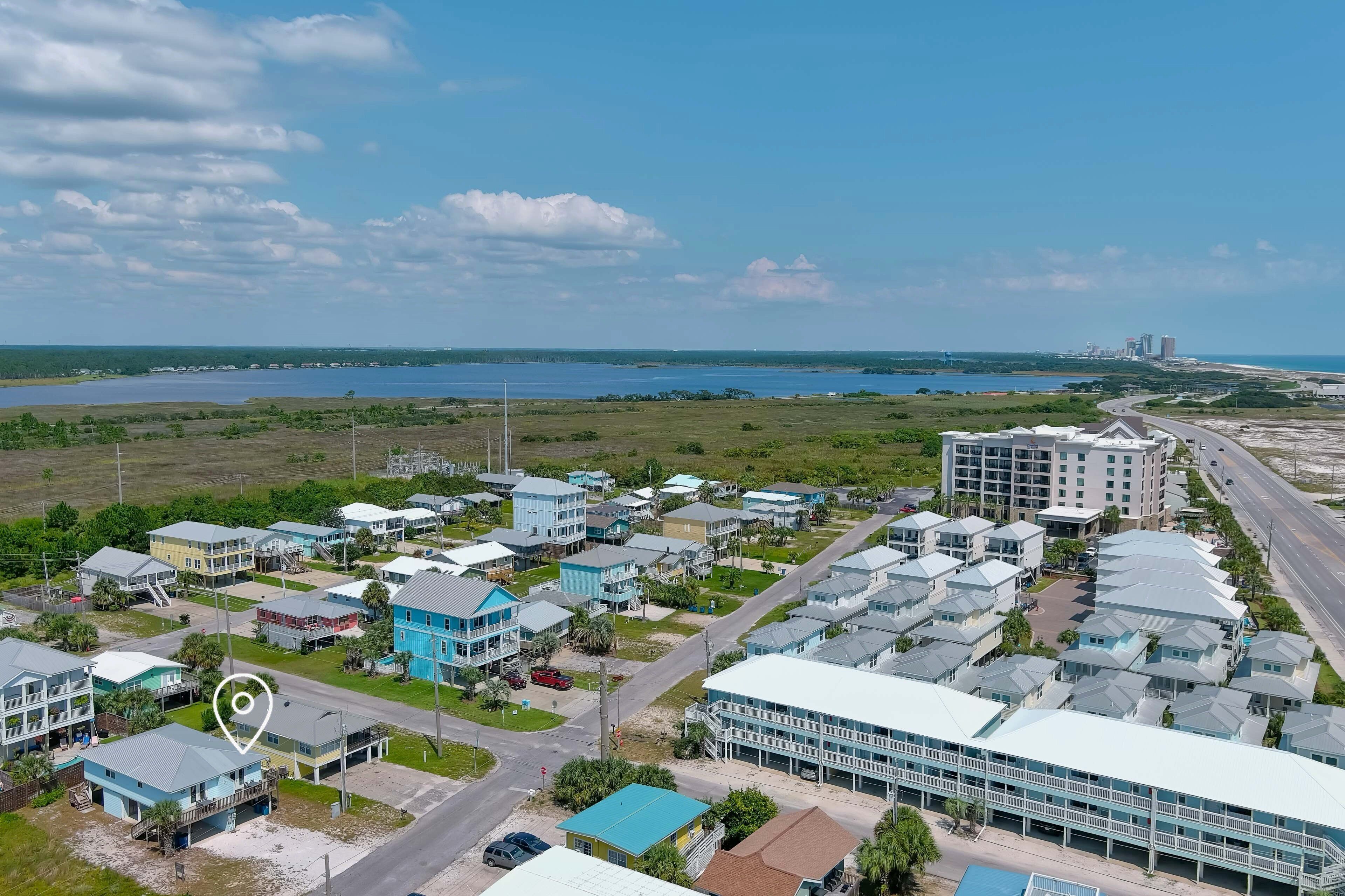 An aerial view of a coastal residential area with multiple buildings, roads, and a body of water in the background.