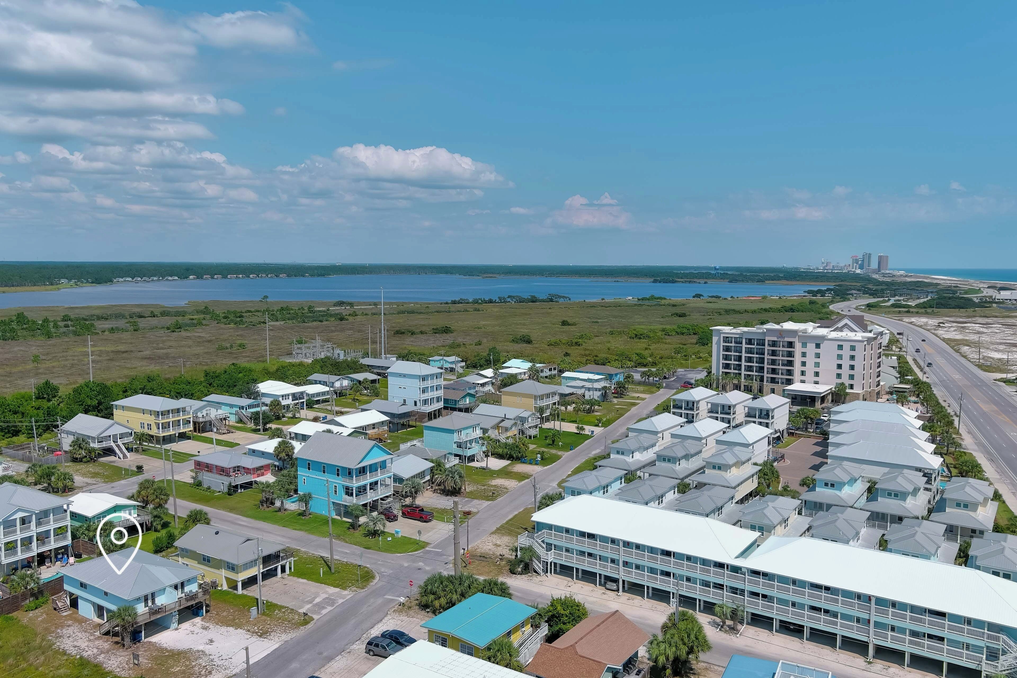 An aerial view of a coastal residential area with multiple buildings, roads, and a large body of water in the background.