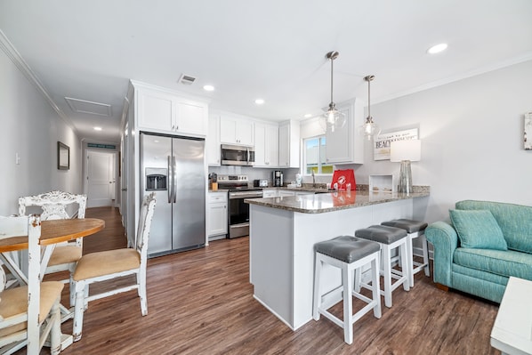 A modern kitchen with white cabinetry, stainless steel appliances, and a central island with bar stools.