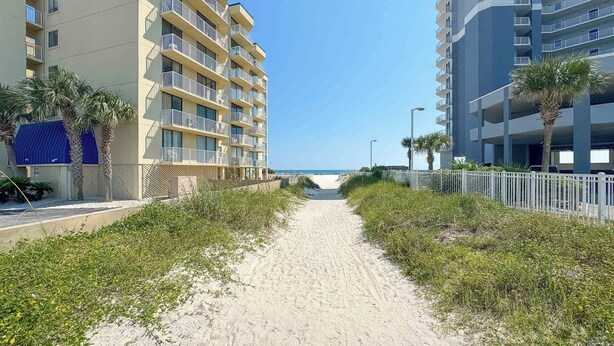 A pathway leading to a beach with a Whaler building on the left and a modern building on the right.