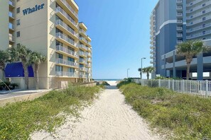 A pathway leading to a beach with a Whaler building on the left and a modern building on the right.