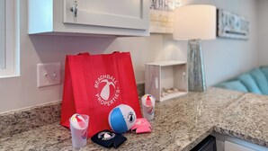 A kitchen counter with a red bag labeled "Beachball Properties," a blue and white beach ball, and two cups with beach-themed designs.