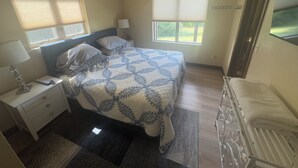 Un dormitorio con cama, mesitas de noche, escritorio, silla y ventanas.