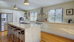 A modern kitchen with a large island, stainless steel appliances, and bar stools. - The Banks: Luxury waterfront retreat on Currambene Creek Jervis Bay (Woollamia)