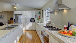 A modern kitchen with white cabinetry, a stainless steel range hood, and a central island with a sink. - The Banks: Luxury waterfront retreat on Currambene Creek Jervis Bay (Woollamia)